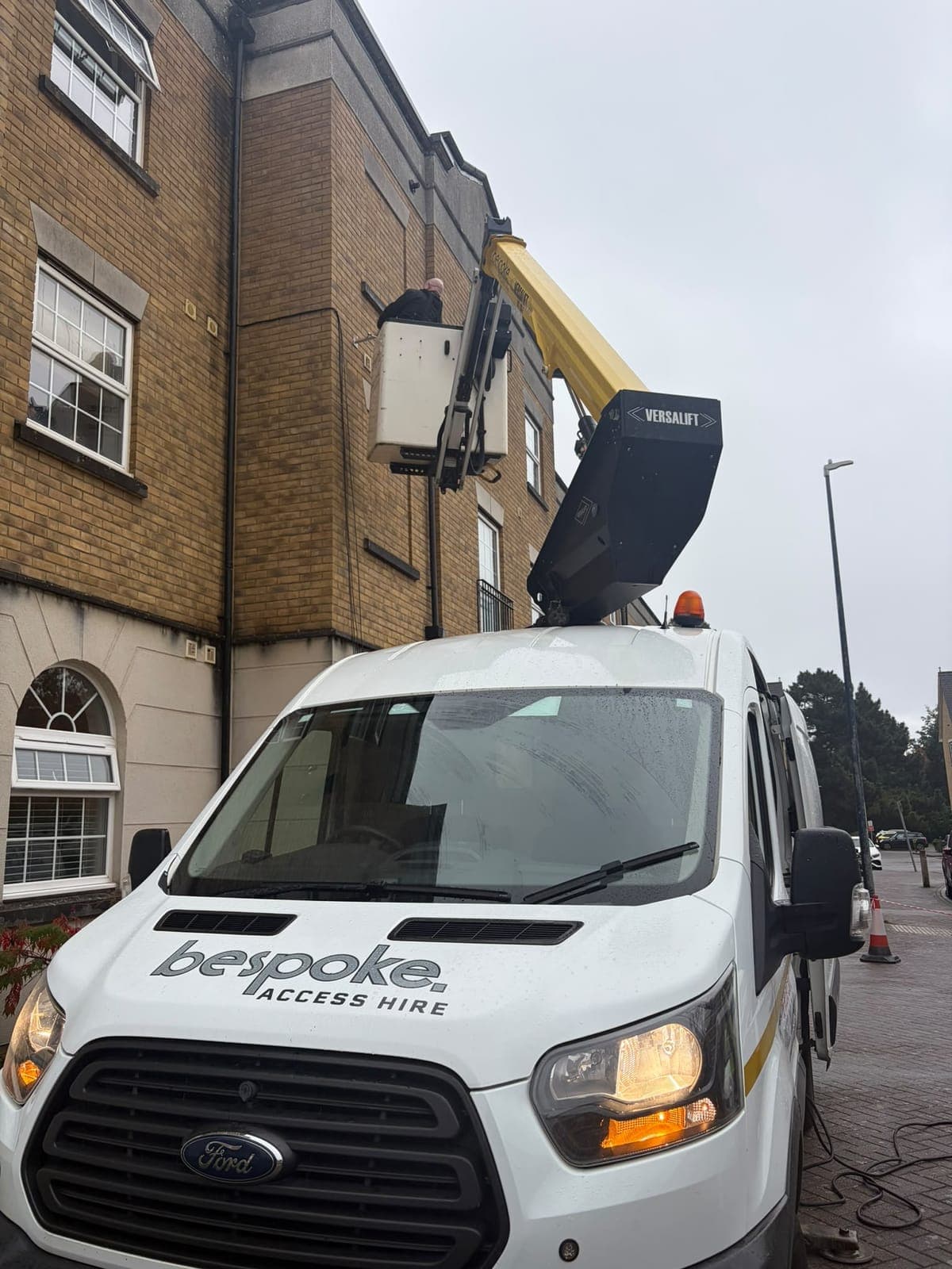 The Versalift boom raised from the Bespoke Access Hire van, with a Bespoke engineer working on the wall of the flats from the basket