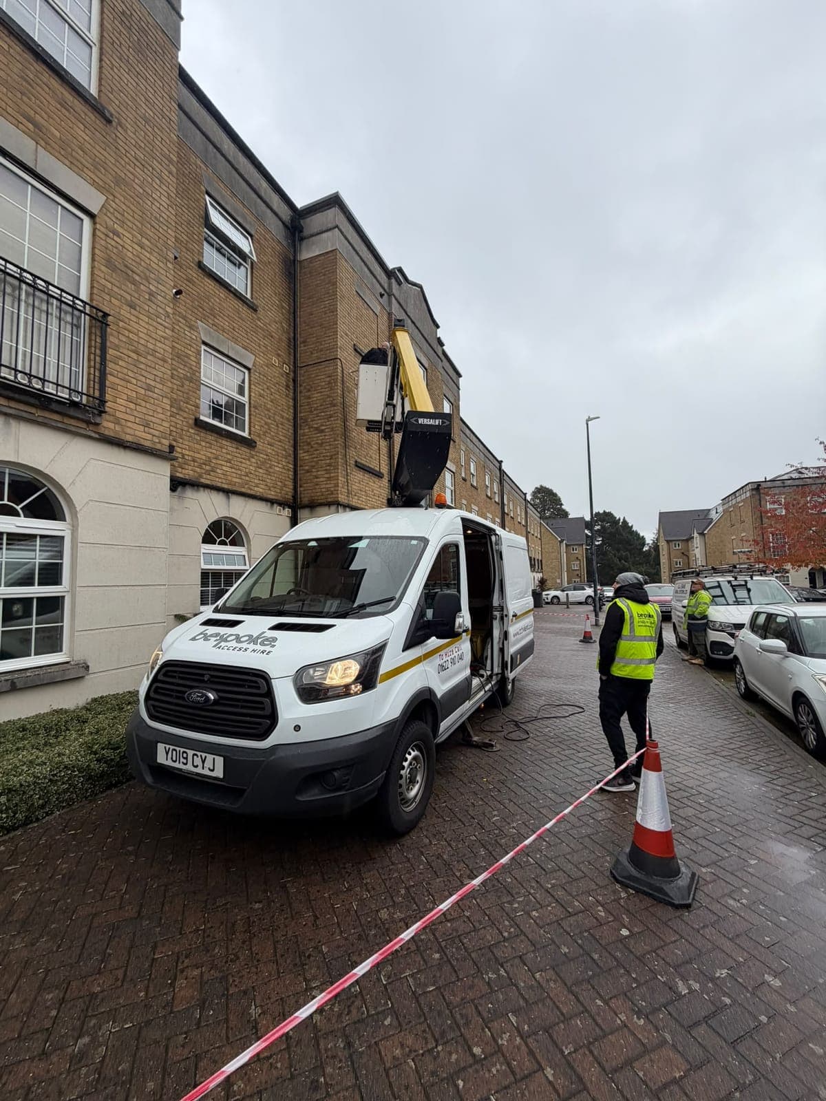 A Bespoke engineer in the cherry picker basket at upper floor height during the satellite relocation, with the Bespoke Access Hire van coned and taped off below