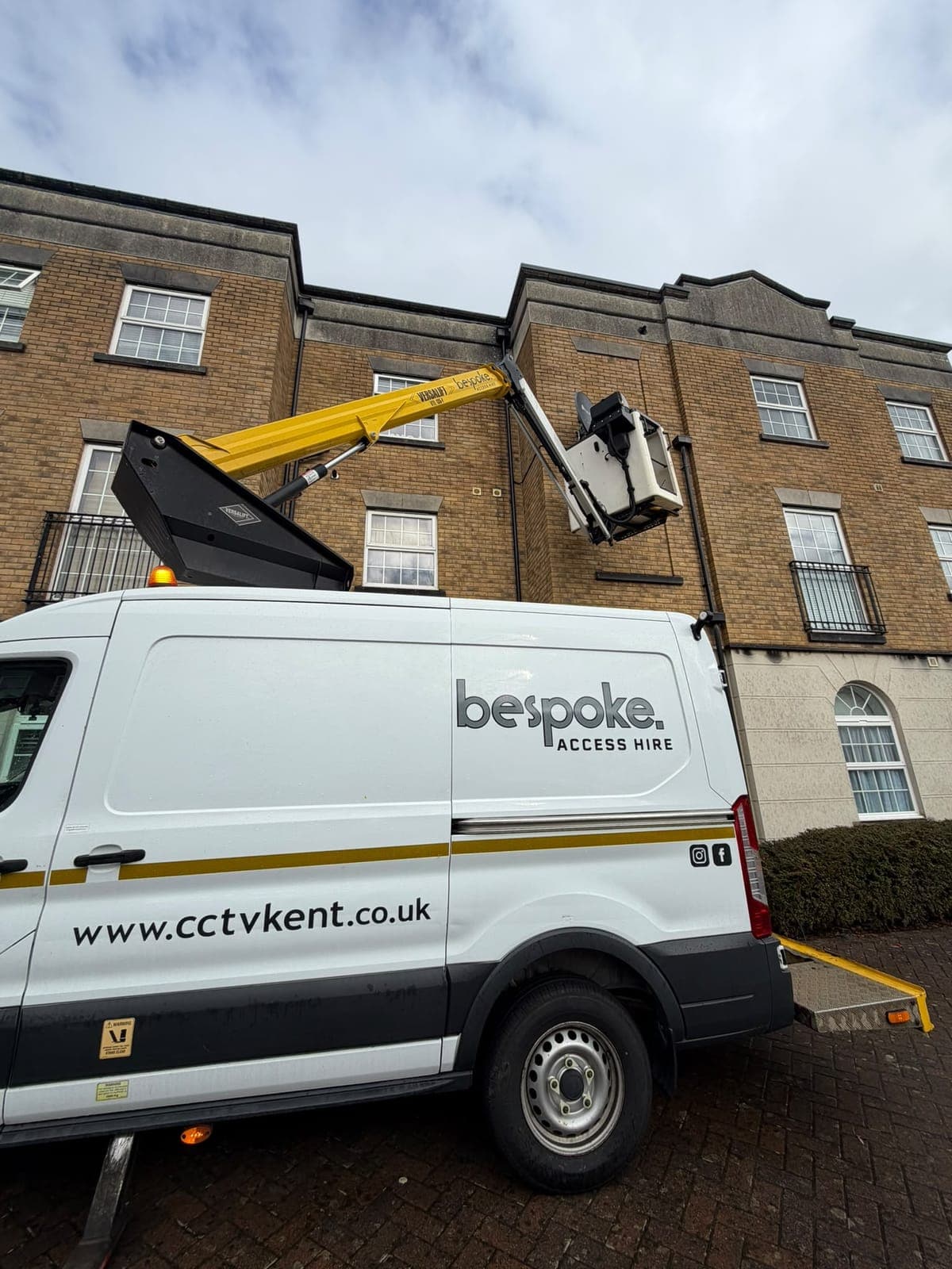A satellite dish in the raised cherry picker basket during an IRS satellite relocation Bespoke carried out on a block of flats, with the Bespoke Access Hire logo on the van's side