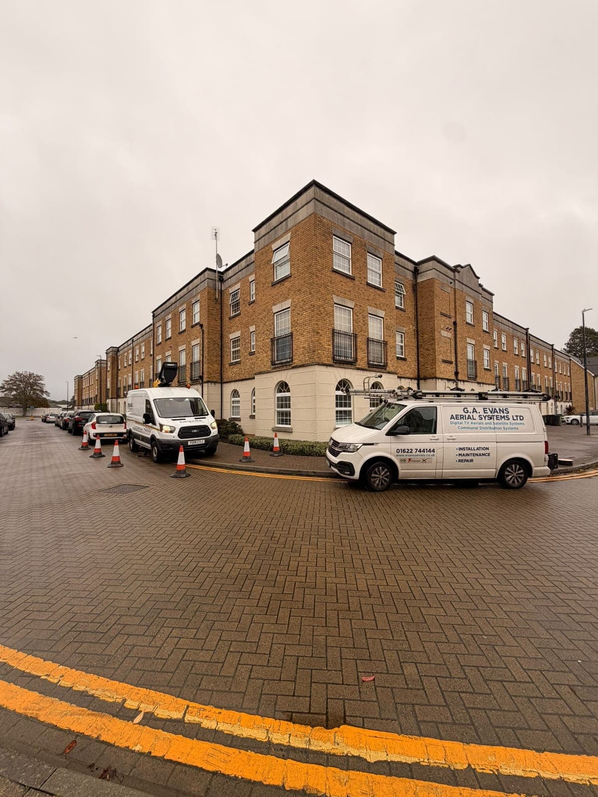The Bespoke Access Hire van parked beside a block of flats with its boom up and cones around the work area