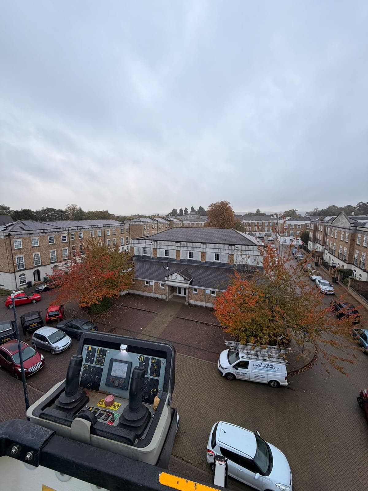 View from the raised cherry picker basket across a residential square, with the platform controls in the foreground