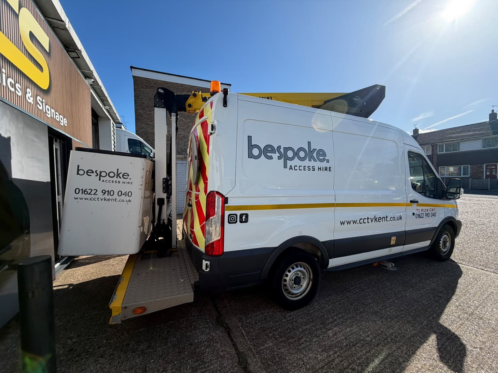 The Bespoke Access Hire van from behind, with the platform basket lowered on its tail lift and the logo on the side