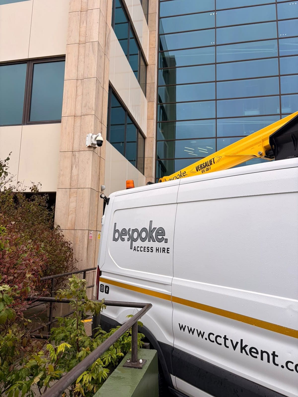 A CCTV dome camera on the stone corner of an office building, with the Bespoke Access Hire van and its Versalift boom alongside
