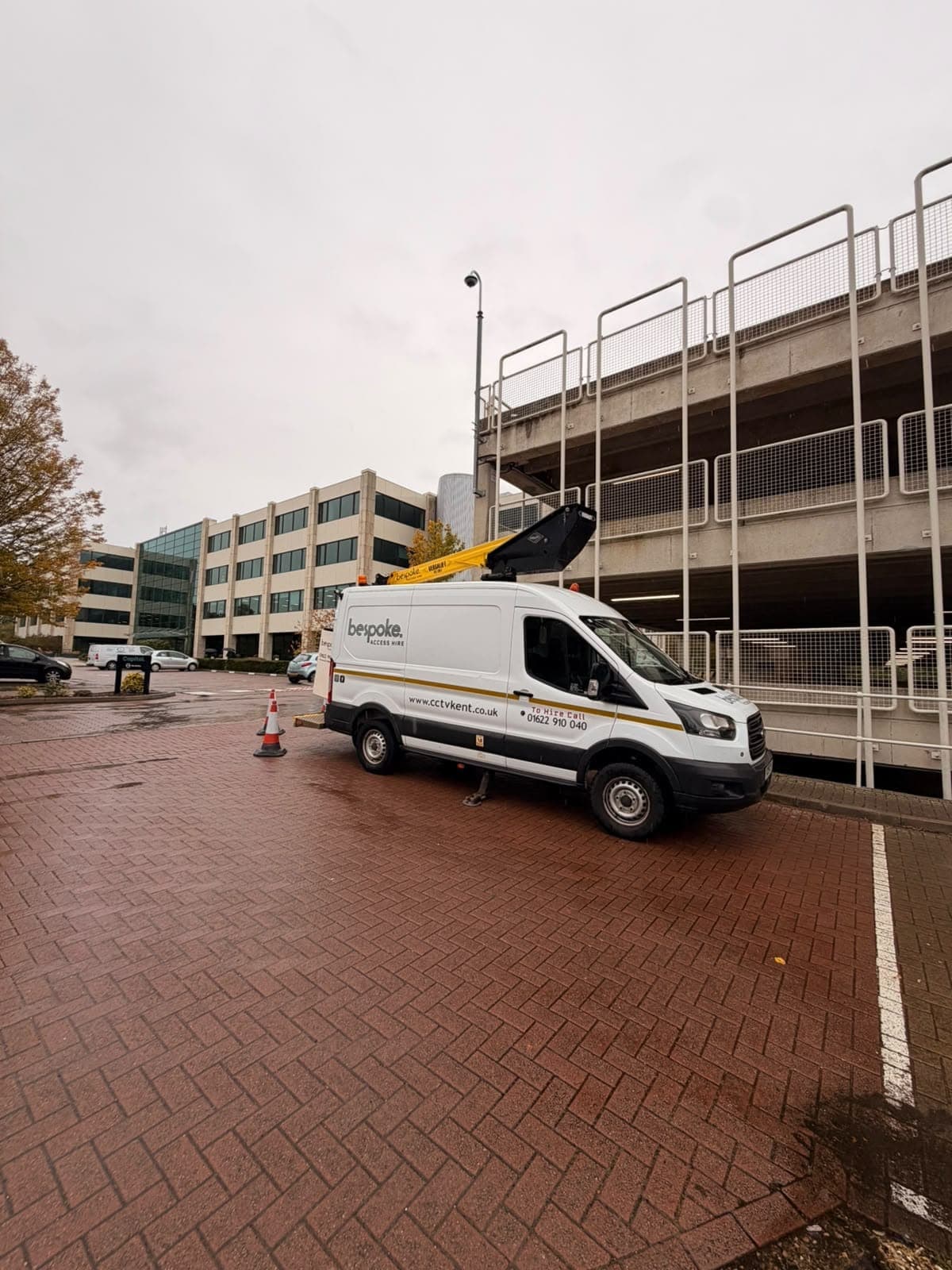 The Bespoke Access Hire van set up beside a multi-storey car park, below a pole-mounted CCTV camera