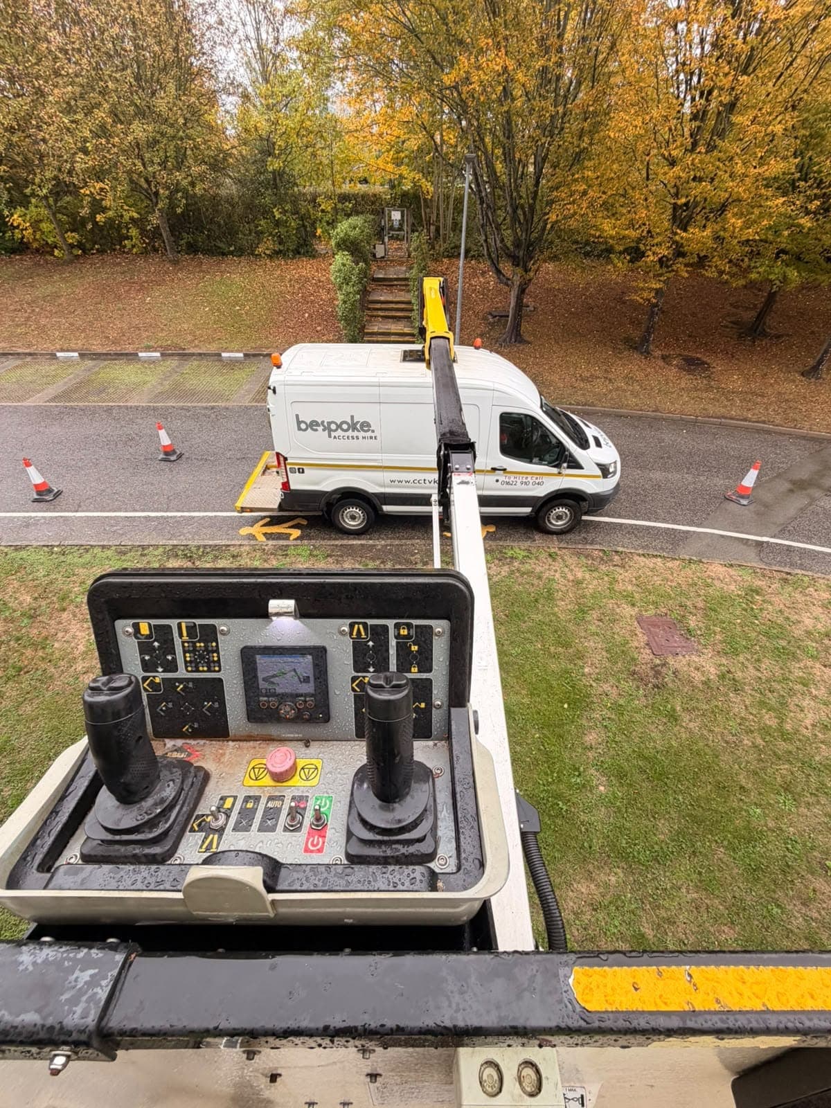 Looking down from the raised cherry picker basket at the Bespoke Access Hire van and its coned off work area