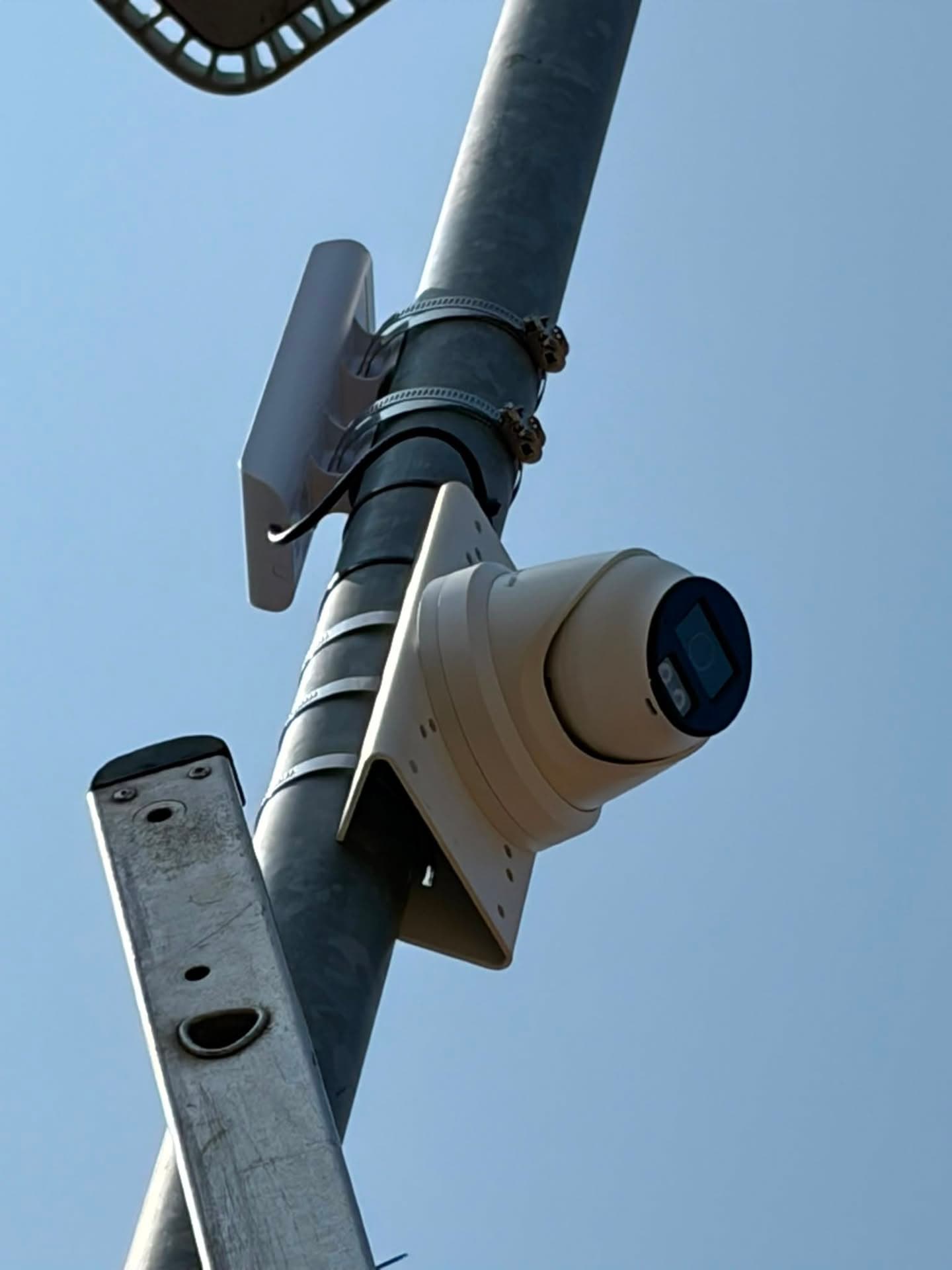 Pole-mounted CCTV camera and wireless link viewed from below against a blue sky