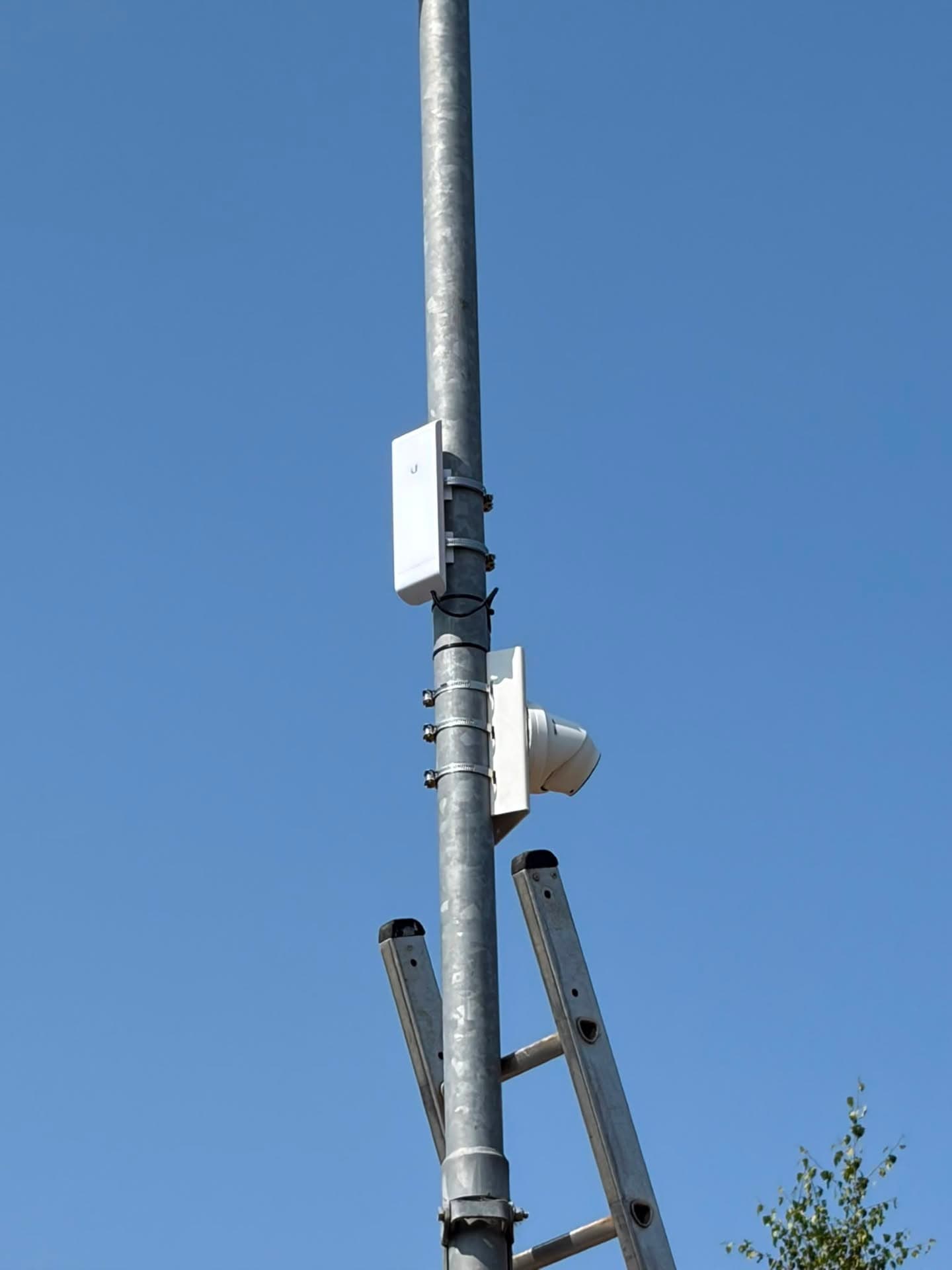 CCTV camera and Ubiquiti wireless link pole-mounted over a car park, installed from a ladder