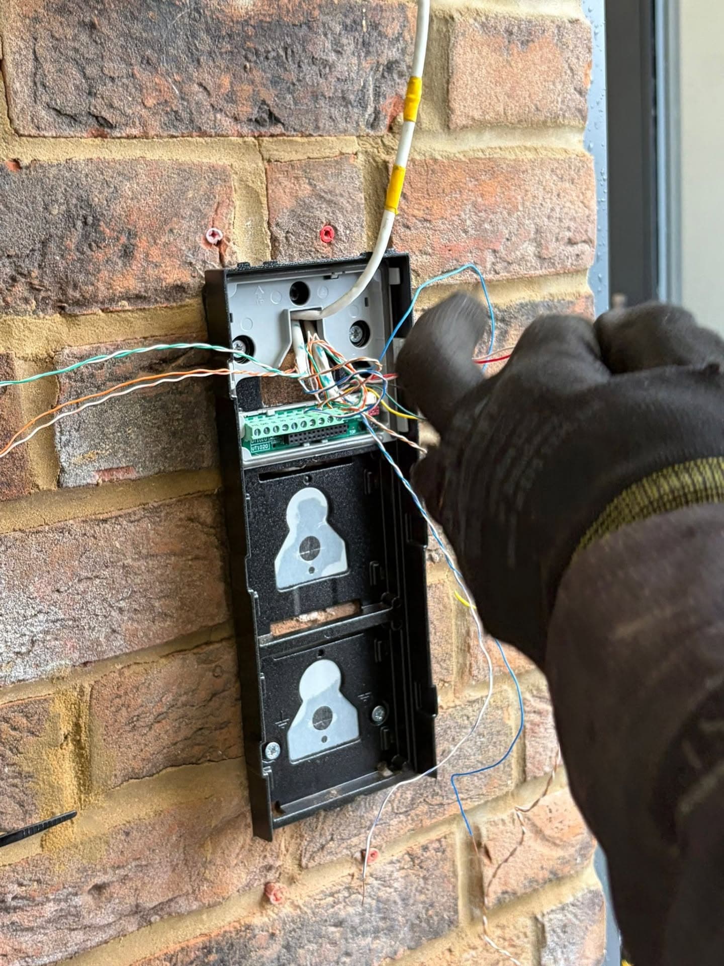 Engineer wiring a video door entry intercom panel into a brick wall
