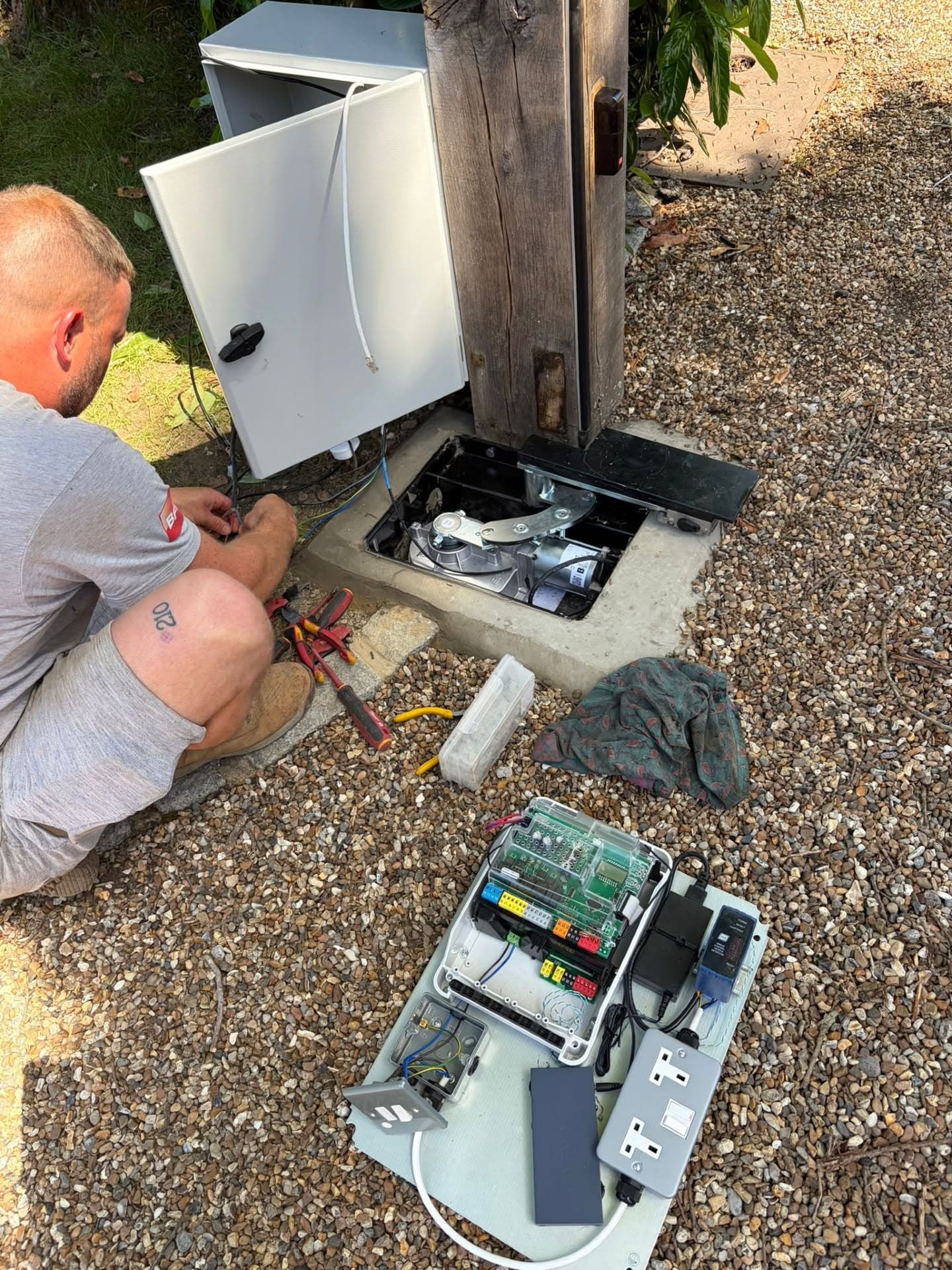 Engineer installing an underground gate motor and automation control board at a driveway gate post