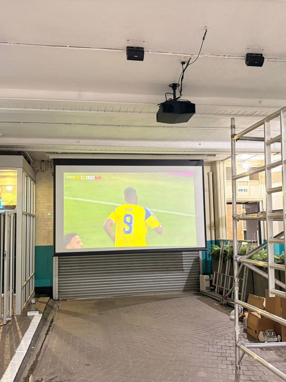 Outdoor drop-down projector screen and speakers installed in a courtyard bar