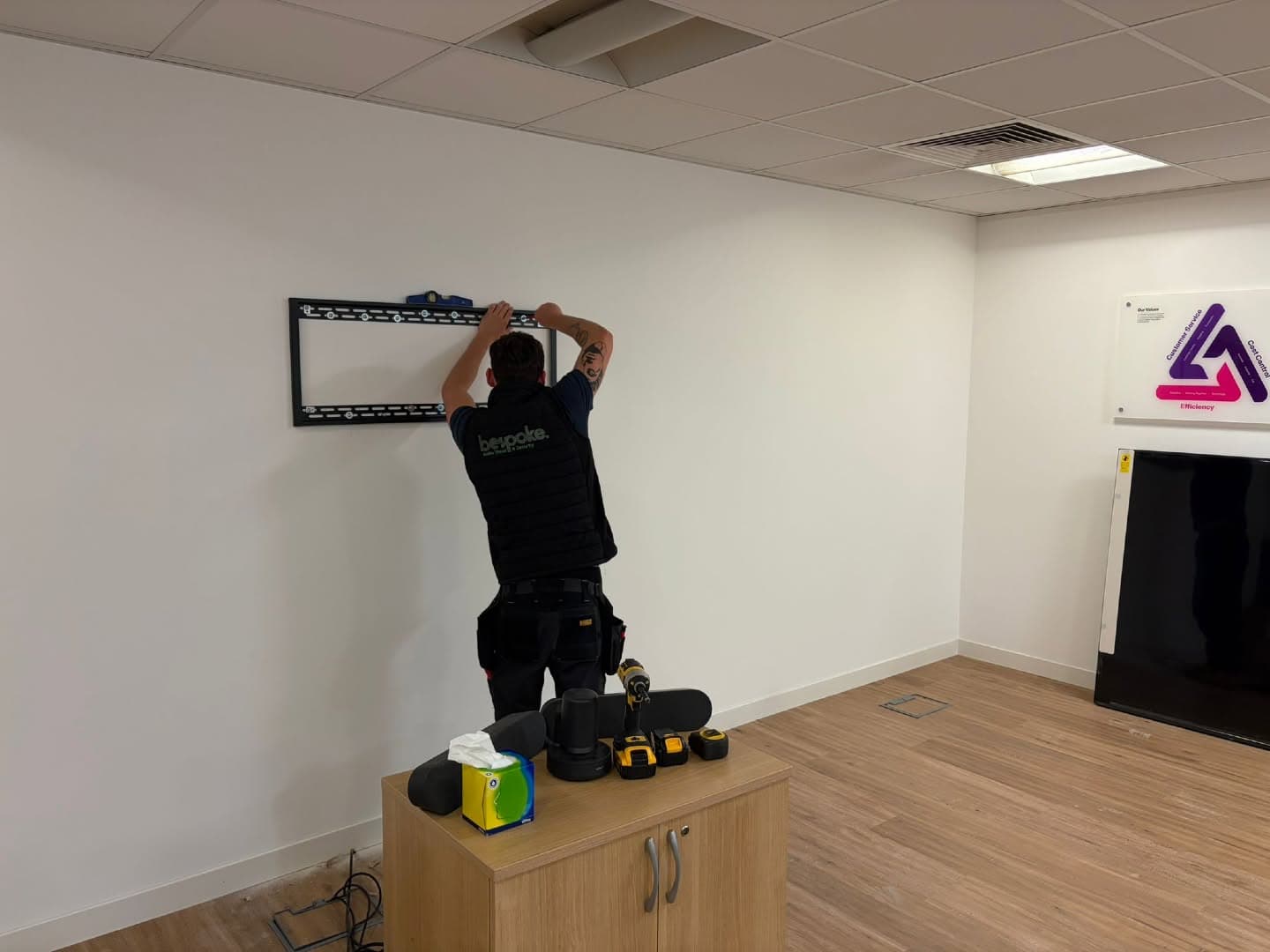 Bespoke AVS engineer levelling a TV wall bracket during an office AV install