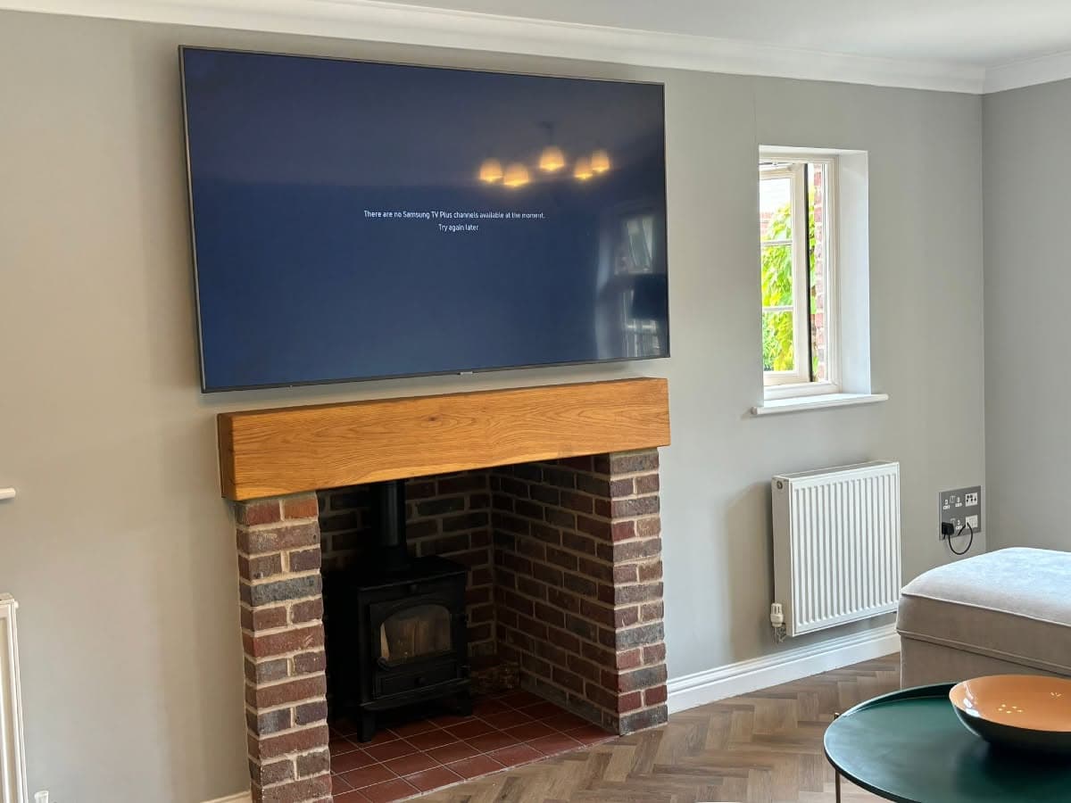 Large TV wall-mounted above an oak beam and brick fireplace