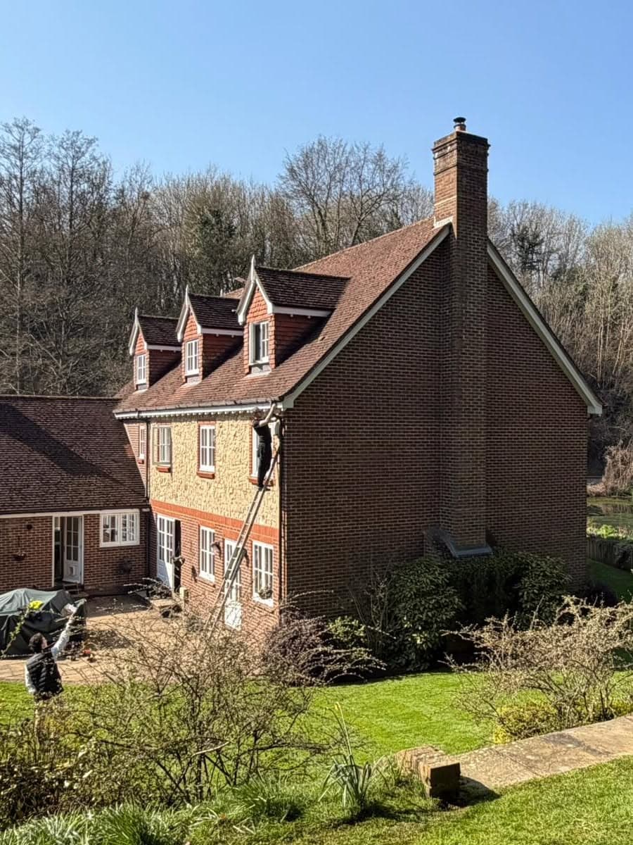 Engineer working at height on the eaves of a Kent country house from an extension ladder